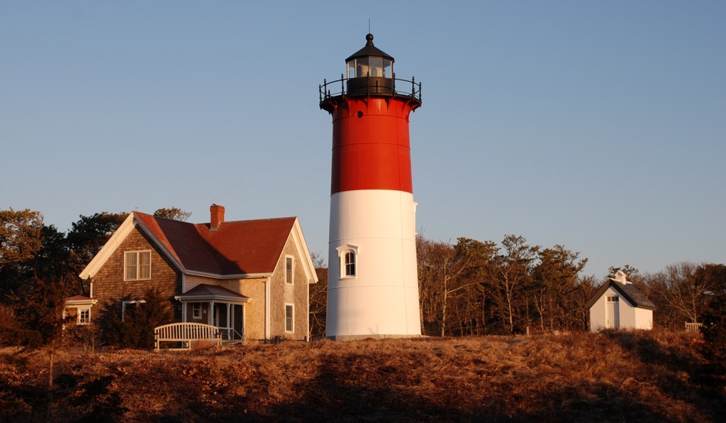 The red and white lighthouse at Nauset Light Beach, with trees and a house behind it
