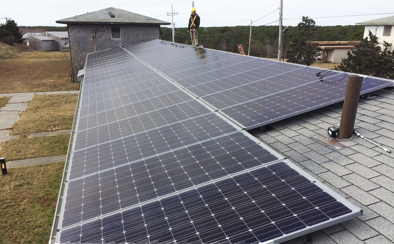 Solar panels on a roof at Cape Cod, with a technician standing above them