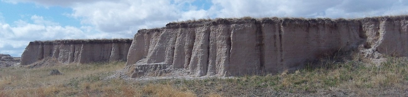 an elevated patch of prairie with steep walls stands above green grasslands.