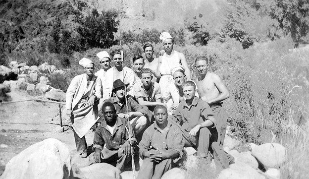 Men of different races sit on rocks in a stream, some with chefs hats on. Men of different races sit on rocks in a stream, some with chefs hats on.