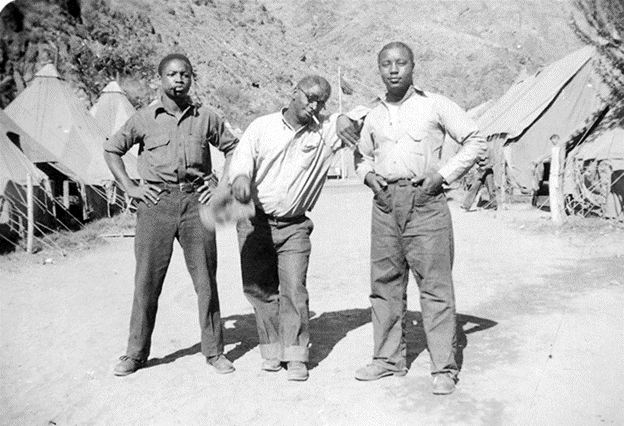 Three Black men stand in between tents.