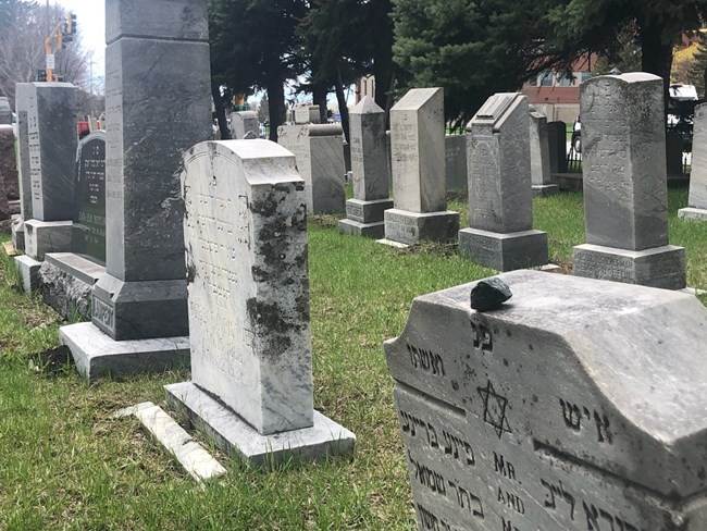 Montefiore Cemetery Grave markers arrayed in rows with inscriptions in Hebrew. A small stone has been placed on the marker in the foreground.