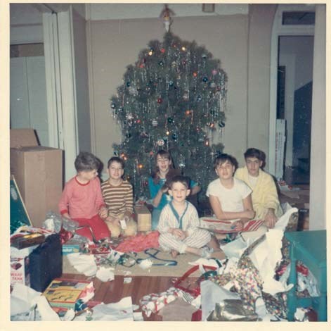 six children sit in front of a Christmas tree surrounded by wrapping paper