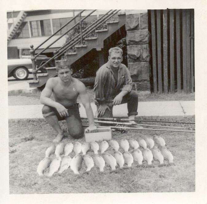 two young men kneel next to rows of dead fish