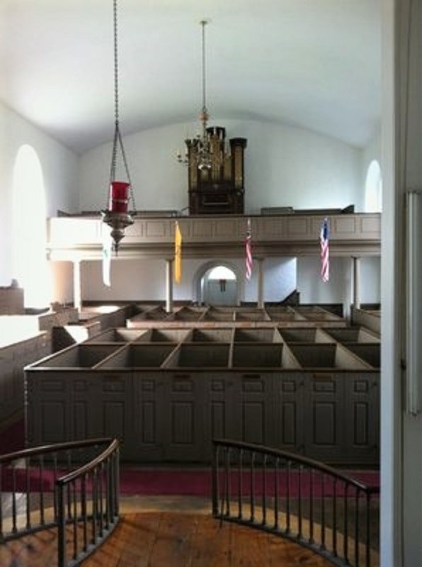 Church interior, with high walled box pews, balcony, organ, and religious lamp