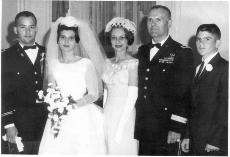 a family portrait from a wedding. A young woman in a wedding dress with her husband in a military uniform aand her parents and brother.
