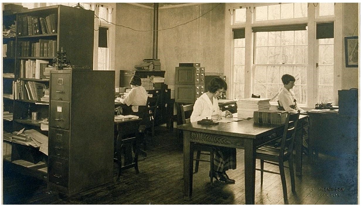 Cold Spring Harbor Laboratory, Eugenics Record Office, interior with workers, circa 1921. Three women sit at desks surrounded by filing cabinets and books.