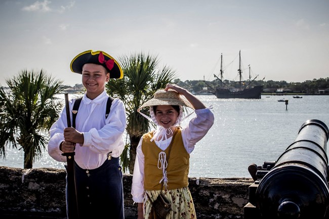 Two kids dressed in colonial clothes standing on gun deck.