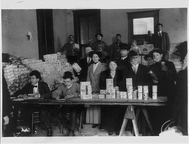 Commissary - Chicago Garment Workers' Strike Several people sit and stand behind a table with boxes of food on it in a black and white photo.