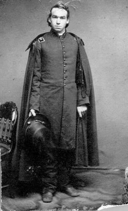 young man standing with his hat in his left hand he is also wearing a cape on his shoulders