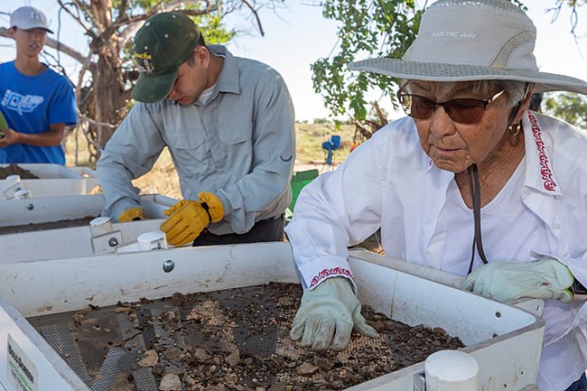 Woman in hat looking at what is caught in an archaeological sieve