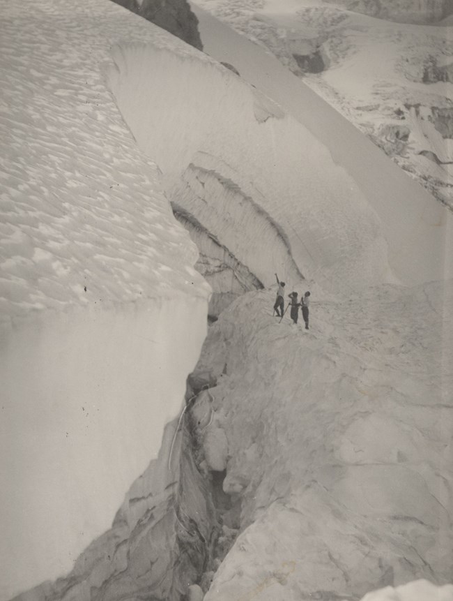 Three people stare up at a towering wall of glacier