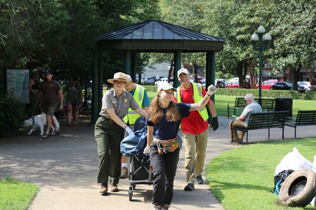 Volunteers, park staff and a Community Volunteer Ambassador pull a wagon down a sidewalk