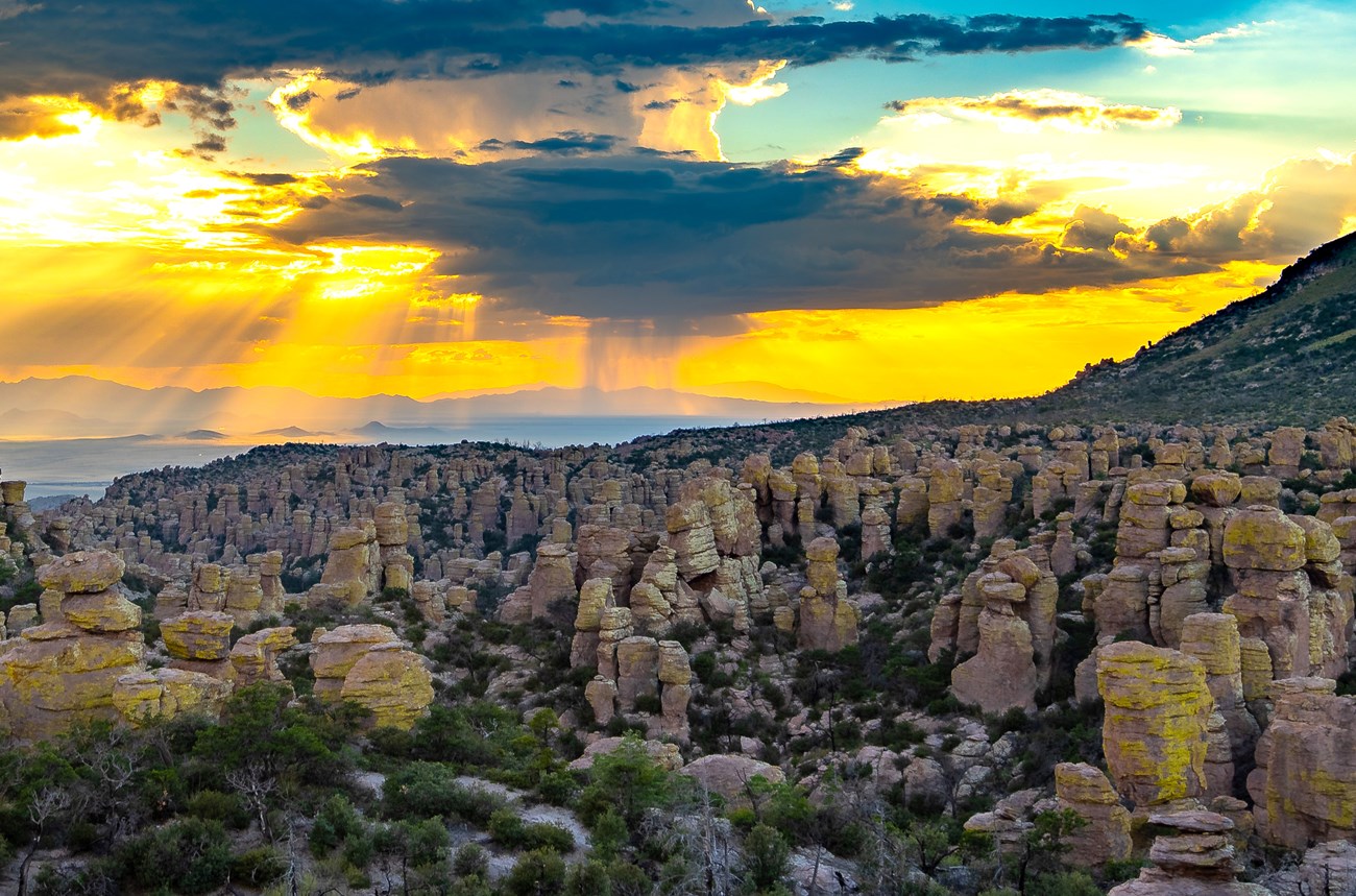 photo of rock towers filling a valley beneath a dramatic sky with clouds and evening sun