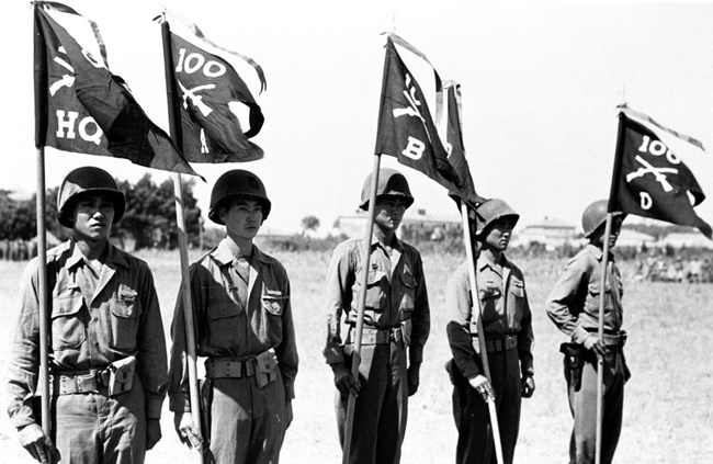 ddr-densho-37-339-mezzanine-7c36ebb270-a Five men in military uniforms holding flags for the 100th Infantry Battalion