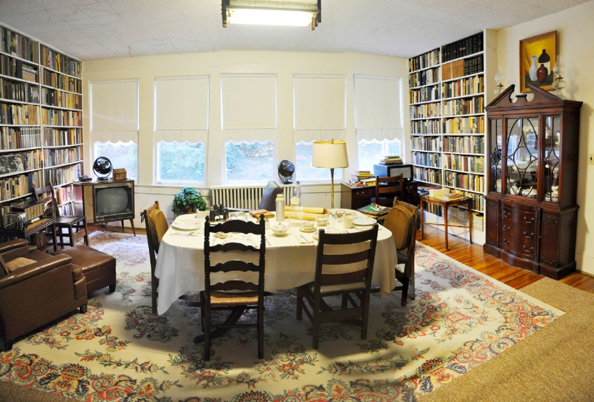 Vintage dining room with table set for dinner, two walls of bookshelves and a bay of five windows on outside wall.