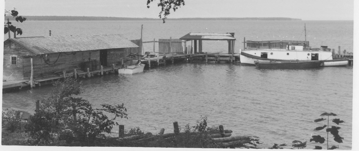Low wooden building and dock on the lake with a boat moored next to it.