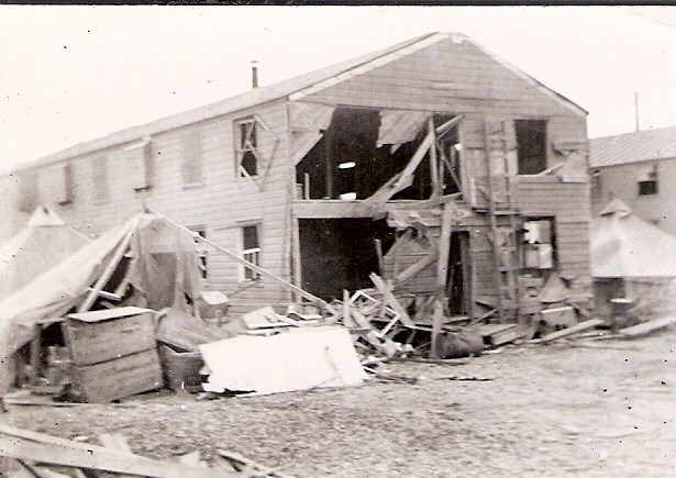Building damaged in Japanese attack on Dutch Harbor Two story wooden building with blown out walls and collapsed tents beside it.