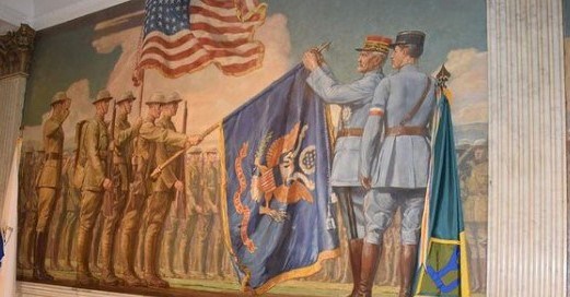 Mural of soldiers standing at attention under an American flag. Two uniformed men are pinning a medal atop a National Guard flag.