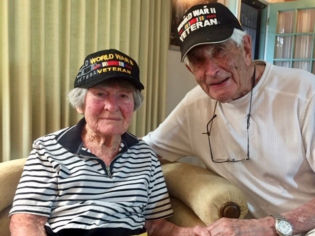 Color photo of a woman and man wearing World War II veteran ball caps.