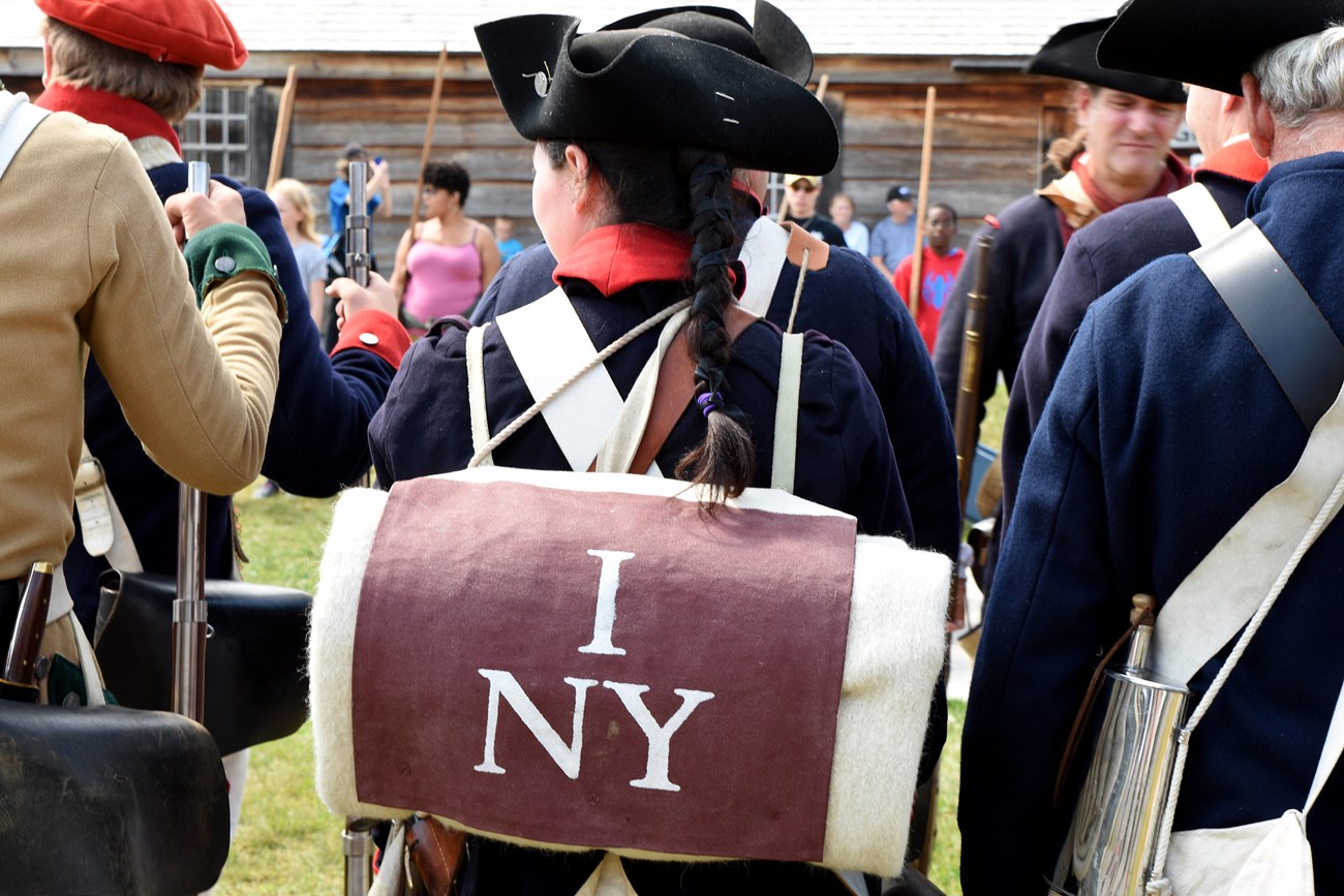 Soldiers in Continental uniform face away from the camera. Their packs on their backs say "1NY"