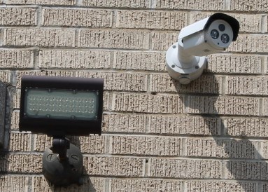 An exterior light and exterior camera mounted on a grey brick wall.
