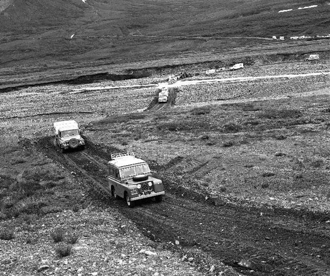 vehicles driving on a narrow gravel road in a tundra meadow