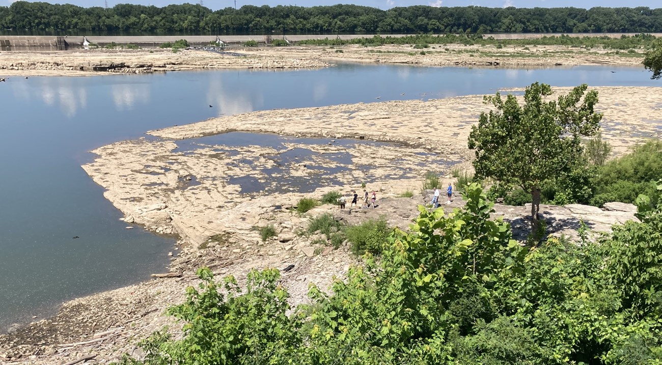 A partially flooded outcrop near river level with a few people walking over it in the distance.