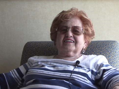 flapan_tybie Older woman with red hair and glasses sits in a chair, smiling.