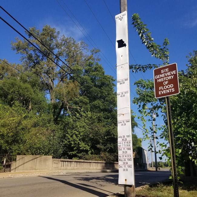 Ste. Genevieve Flood Gauge A white sign with black lines showing flood levels stands next to a concrete bridge