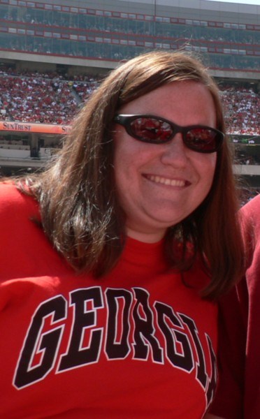 A woman with sunglasses at a football game and Georgia on her sweatshirt.