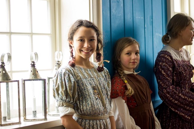 A smiling girl wearing an 1840s style dress. Her hair is in two braids.