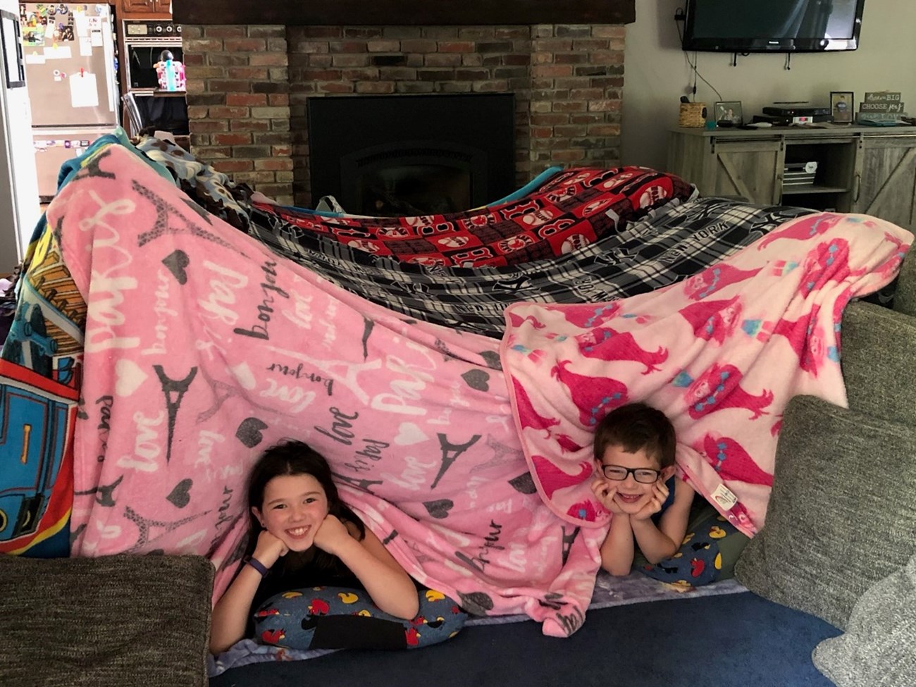 Two kids in a fort made of blankets.