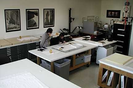 At a large clean table, two people look at something through a microscope.