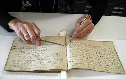 Bare hands are holding tools like tiny awls to the old books surface.