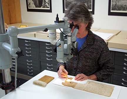 Looking through a microscope, a woman rubs a small brush over the pages.