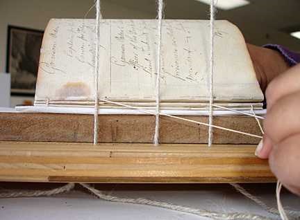 A close-up of the old book's spine with the 3 strings now sewn through the edge.