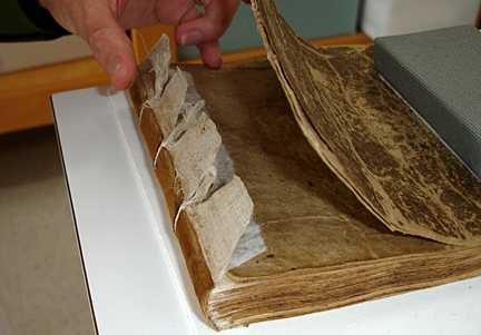 A hand thumbs through the severely torn cover of the old book.