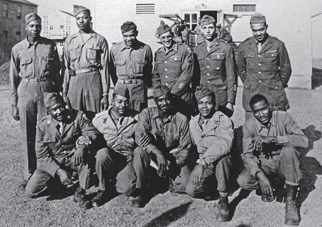 a group of 11 uniformed Black military members pose in a historic scene.