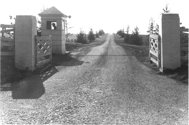 The Eisenhower Farm front lane, complete with gates and a guard booth. a road with wooden gates open, on the left side a guard booth with a guard.