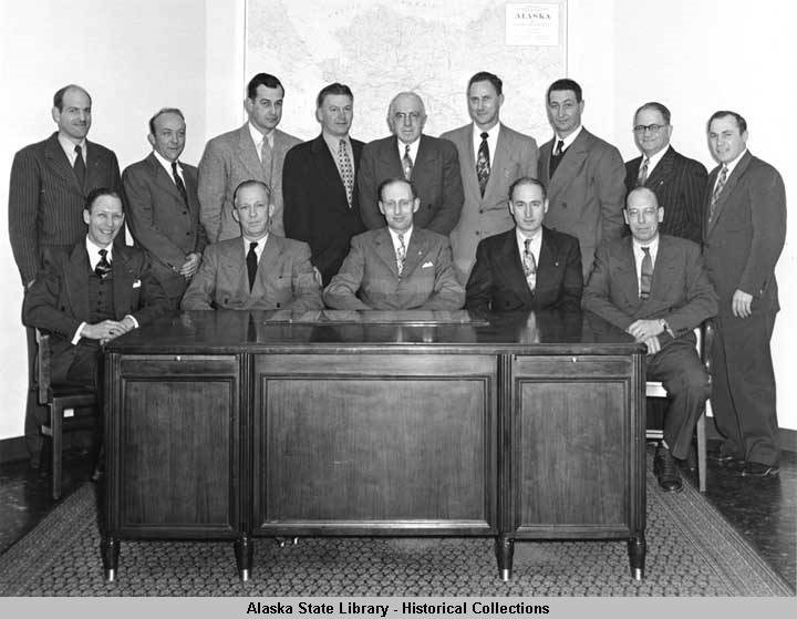 g-1 about a dozen men in business suits posing for a photo behind a desk