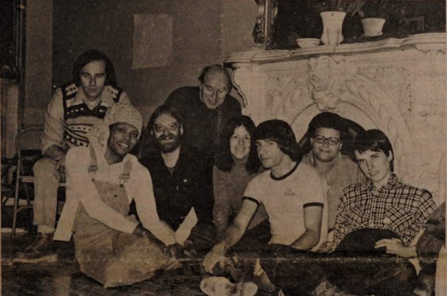 eight people of varying ages sitting in front of a fireplace.