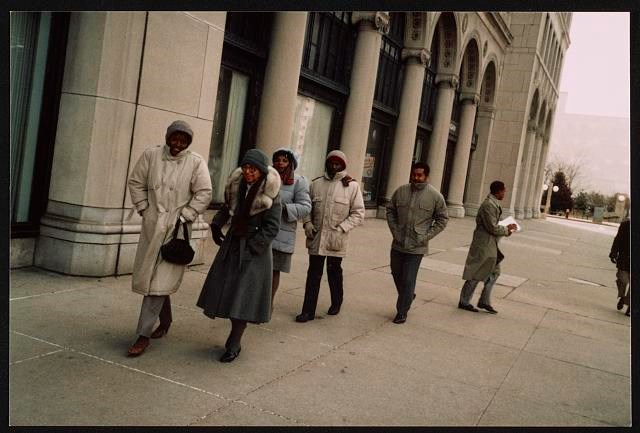 People in coats on a sidewalk outside of a building.