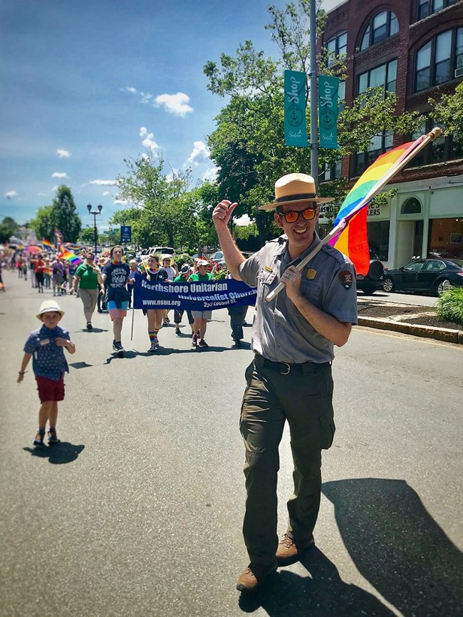 Park ranger walking in a pride parade holding a rainbow flag