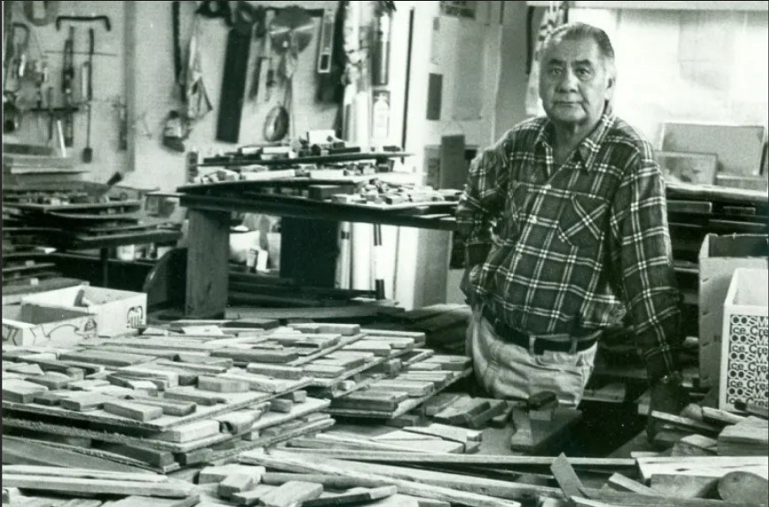 A man in a room, surrounded by pieces of wood.