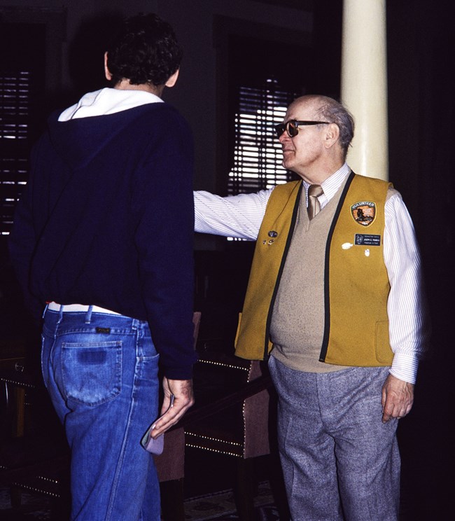 Volunteer in gold vest Man in gold vest points in conversation with another man