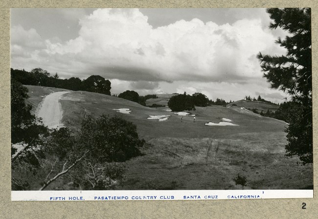 black and white of hill with sand traps and golfers on it