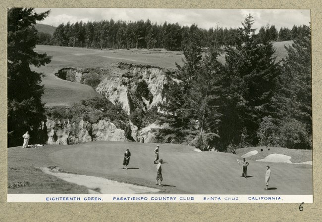 black and white of group of golfers standing on flat area above a valley