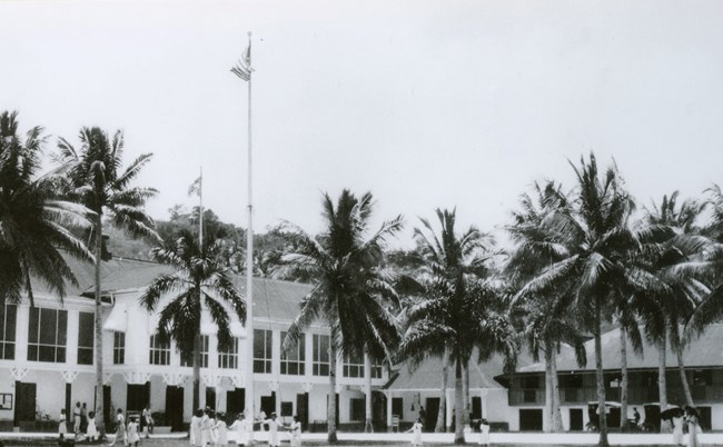 Government House, Guam, 1930 People play under palm trees in the courtyard of a large white house.