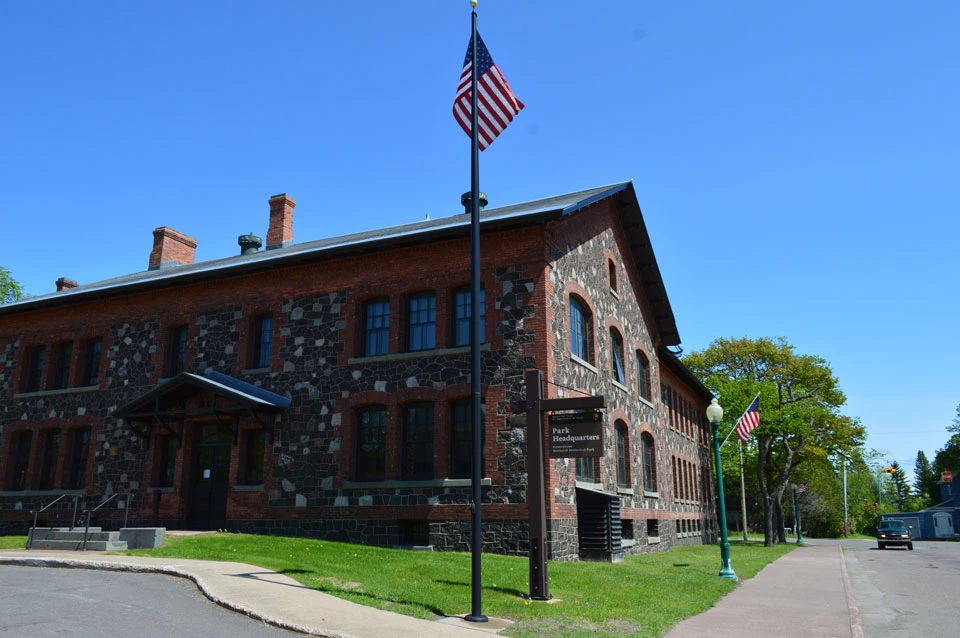Keweenaw NHP Headquarters summer scene of a two story brick and stone building with a sidewalk leading to the entrance